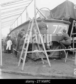 Wrens treno per Nuovo lavoro - Formazione per nave meccanica delle donne del Royal Naval Service, Inghilterra, Regno Unito, 1943 Donne del WRNS stand su tavole bilanciato su scale a pioli per il riconoscimento di vernice lettere e numeri sul lato di una landing craft come parte della loro formazione per diventare nave meccanica (LC), probabilmente a Slough Governo Centro di formazione. Le lettere sono state disegnate in scala in gesso e vengono riempiti con un pennello. Una volta elaborato, il lavoro sarà svolto utilizzando matrici, per risparmiare tempo. Un istruttore (in camice bianco), può essere visto in background controllando il loro lavoro. Foto Stock