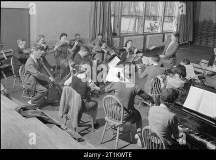 Leader giovanili all'Impington College- Education and Training in Cambridgeshire, Inghilterra, Regno Unito, aprile 1944 come parte di un corso di una settimana per i membri del servizio giovanile, Miss e Smith (a destra) conduce un gruppo di studenti di musica durante una conferenza di Cyril Winn su "The Dance Idiom". Gli studenti suonano violini, violoncelli e pianoforte durante la lezione all'Impington Village College. La didascalia originale afferma che "Miss Smith è responsabile della musica junior al Dulwich College e prende una classe orchestrale per il London County Council". Foto Stock