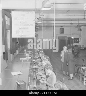 Telefono automatico Cambio - Comunicazioni in tempo di guerra, London, England, Regno Unito, 1945 Una vista generale delle donne gli operatori a lavorare in interruttore manuale stanza a un sistema automatico di scambio telefonico. Secondo la didascalia originale, "lo scambio ha una scheda manuale con 13 posizioni trattare con 'Tol' traffico, 26 con assistenza ordinaria del traffico e 1 per tamponamento circuiti guasti'. Un ampio bordo sospese dal soffitto ha i numeri di telefono per il fuoco, la polizia e i servizi di ambulanza scritto su di esso, in modo che gli operatori per il trasferimento di chiamate attraverso i numeri corretti. Foto Stock