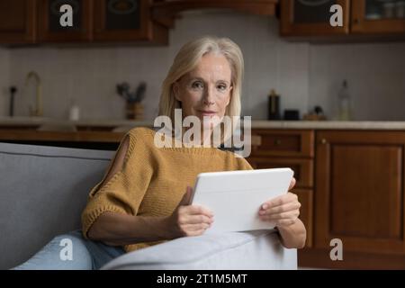 Donna anziana sicura e positiva che usa il tablet a casa Foto Stock