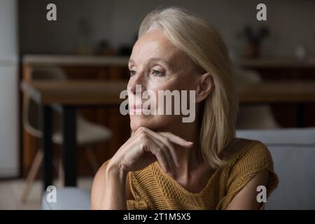 Bella e solitaria signora matura bionda seduta sul divano di casa Foto Stock