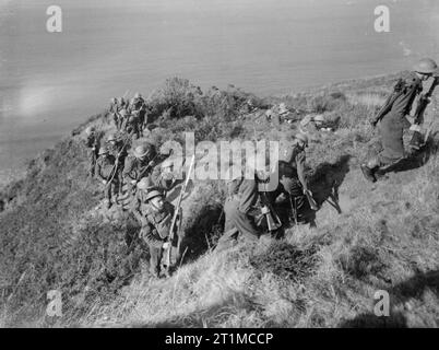 L'Esercito Britannico nel Regno Unito 1939-1945 uomini del 2° London Irish fucili avanza con baionette fisso dopo arrampicata sulle rocce durante il corso di formazione al Little Haven vicino a Haverfordwest. Foto Stock