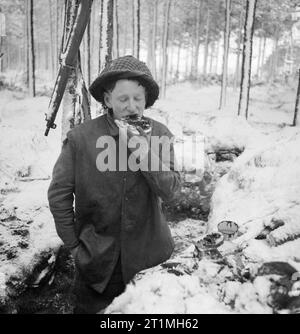 Un soldato britannico mangia il suo pasto di mezzogiorno in una trincea nella neve, mentre manning parte della linea anteriore lungo il fiume Maas in Olanda, 8 gennaio 1945. G privato Carnally mangia il suo pasto di mezzogiorno in una trincea nella neve, mentre manning parte della linea anteriore lungo il fiume Maas in Olanda, 8 gennaio 1945. Foto Stock