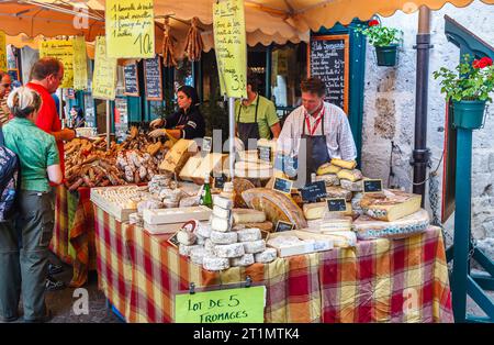 Bancarelle di formaggi e carni e mostre di prodotti locali in un mercato all'aperto di Annecy, Francia, con un'ampia selezione di formaggi duri e morbidi Foto Stock