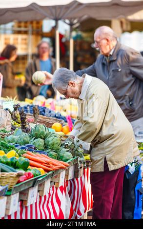 Una donna francese locale acquista una selezione di verdure fresche esposte in vendita su un bancone di una bancarella ad Annecy, in Francia Foto Stock