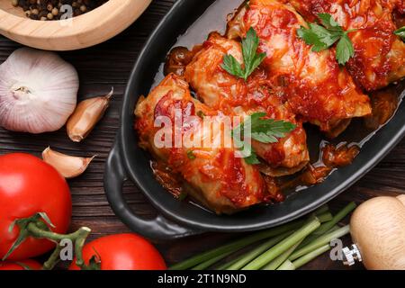 Deliziosi involtini di cavolo ripieni cucinati con salsa di pomodoro e ingredienti su un tavolo di legno, piatti Foto Stock