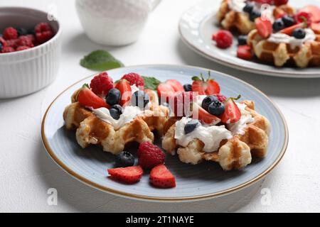 Deliziosi waffle belgi con frutti di bosco freschi e panna montata sul tavolo bianco Foto Stock