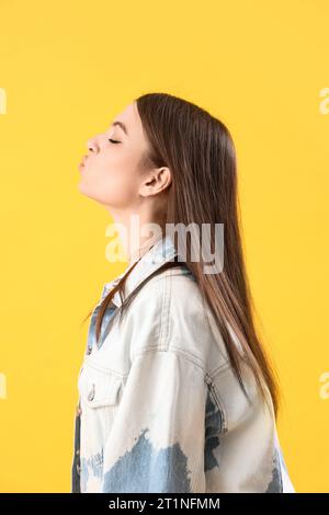 Giovane donna che soffia bacio su sfondo giallo Foto Stock