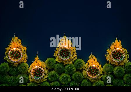 Lampade diya in argilla a forma di fiamma accese per celebrare il festival Diwali con fiori colorati su sfondo blu scuro. Foto Stock