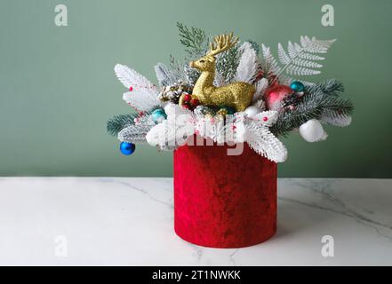 Composizione natalizia in scatola rossa con abete rosso, felce per decorazione tavola. Mazzetti innevati con rocchetti, renne in bella confezione, assemblati da un Foto Stock