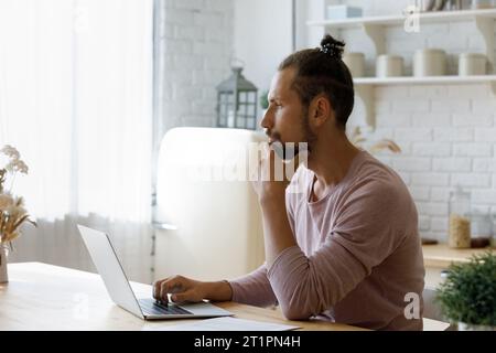 Uomo freelance Millennial serio e premuroso che lavora con un notebook Foto Stock