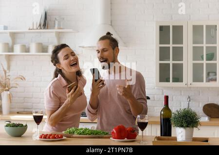 Coppia felice entusiasta con canzoni che cucinano in cucina in casa Foto Stock