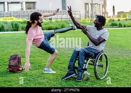 Due diversi amici all'aperto: Un uomo con una gamba protesica equilibra giocosamente, mentre l'altro, su una sedia a rotelle, raggiunge con gioia. Il loro legame radia Foto Stock