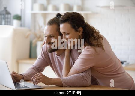 Coppia felice che utilizza il servizio online su un laptop in cucina Foto Stock