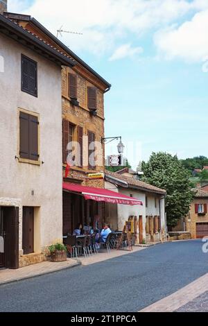 Persone sedute a un tavolo in un ristorante del villaggio locale, un vecchio edificio storico in pietra dorata a due piani con finestre a persiane a Charnay, in Francia Foto Stock