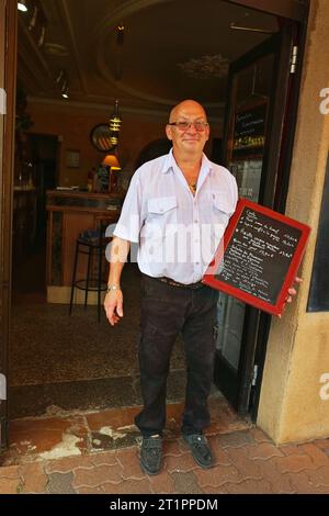 Lo chef Michel Herbet si trova in piedi con un menu presso il suo bar e ristorante pizzeria le Petit BAGNOLAIS. Foto Stock