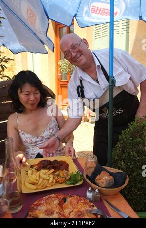 Lo chef Michel Herbet serve un pasto all'aperto nel suo bar-ristorante-pizzeria le Petit BAGNOLAIS nel villaggio di Bagnols in Francia Foto Stock