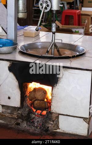 Utilizzo di marmellate di cocco per riscaldare la miscela di caramelle di cocco in una fabbrica di caramelle di cocco di Mekong River, Vietnam. Foto Stock