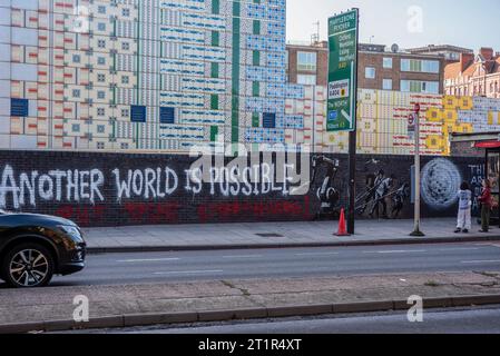 Londra, Regno Unito. 14 ottobre 2023. Due persone sono viste guardare i potenziali graffiti di Banksy sul muro. Un potenziale nuovo murale di Banksy è apparso lunedì a Londra vicino alla stazione della metropolitana di Edgware Road. L'illustrazione mostra tre figure che tirano via un gigantesco braccio robotico accompagnato dalle parole: "Un altro mondo è possibile. Metti la vernice ovunque!". Credito: SOPA Images Limited/Alamy Live News Foto Stock