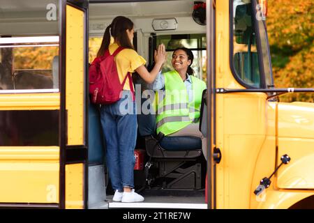 Una bambina allegra che dà cinque alle donne sorridenti dello scuolabus Foto Stock