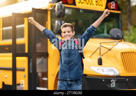 Felice eccitato Preteen Boy Raising Arms mentre si trova vicino alla Yellow School Bus Foto Stock
