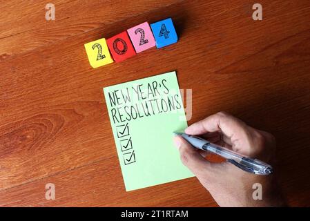 Immagine dall'alto di cubi di legno con il numero 2024 e una persona che scrive i propositi di Capodanno su una nota adesiva. Foto Stock