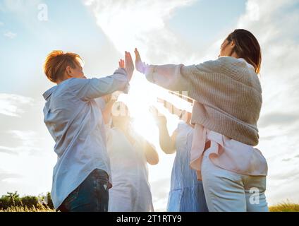Ritratto di quattro donne ridenti allegre che tengono le mani su fare cinque alti durante la camminata all'aperto. Guardano la fotocamera. L'amicizia della donna, nat Foto Stock