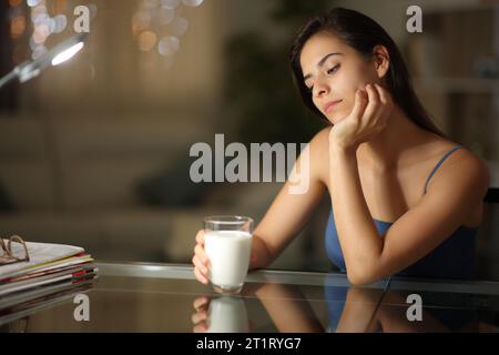 Donna pensiva che guarda il suo bicchiere di latte di notte a casa Foto Stock