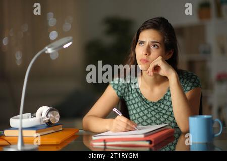 Studente preoccupato che pensa di scrivere un lavoro la notte a casa Foto Stock