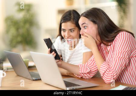 Due telelavoratori stupiti che controllano i contenuti del telefono a casa Foto Stock