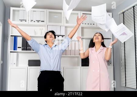 Felicissimo uomo d'affari e donna asiatica sorridendo mentre lanciava documenti in aria con felicità e celebrazione del successo in ufficio - un luogo di lavoro di successo e divertente nel lavoro aziendale. Foto Stock