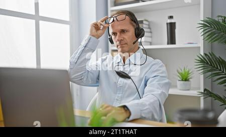 Uomo di mezza età stanco di lavoro si toglie gli occhiali dopo un'intensa videochiamata di lavoro in ufficio Foto Stock