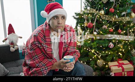 Giovane ispanico che beve caffè per festeggiare il natale a casa Foto Stock