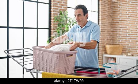 Uomo di mezza età che tiene i vestiti di cesto nella lavanderia Foto Stock