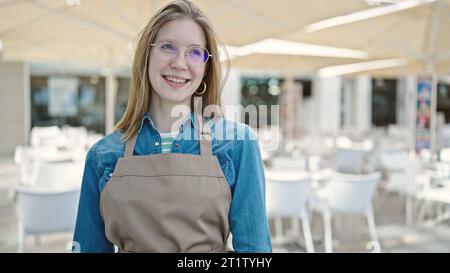 Cameriera giovane donna bionda sorridente fiduciosa in piedi sulla terrazza della caffetteria Foto Stock