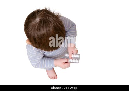 Il bambino ha aperto il cassetto con pillole e medicine, isolato su sfondo bianco. Bambino che tiene in mano un pacchetto di pillole in casa Foto Stock