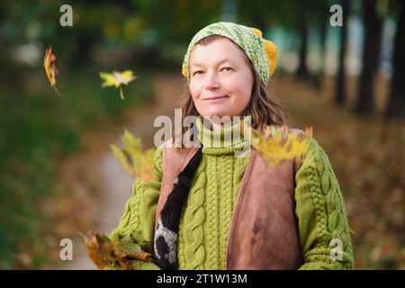 Ritratto di una bella donna con una giacca verde e un cappello a maglia con foglie autunnali. Ritratto di una donna di 52 anni Foto Stock