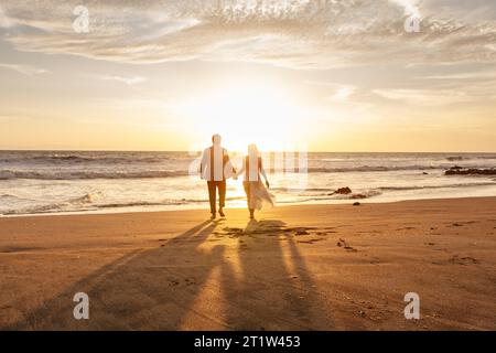 Coppia romantica che passeggia a piedi nudi sulla spiaggia al tramonto Foto Stock