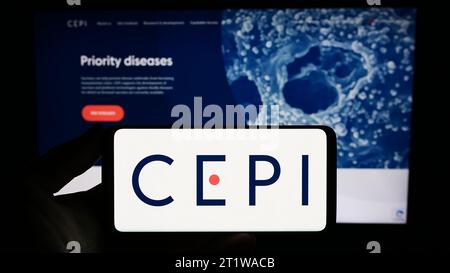 Persona che possiede uno smartphone con il logo della Coalition for Epidemic Preparedness Innovations (CEPI) davanti al sito web. Concentrarsi sul display del telefono. Foto Stock