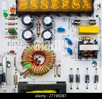 Primo piano dei componenti elettronici sulla scheda a circuito stampato bianca. Bobina toroidale e vari condensatori, fusibile elettrico e trimmer resistore o diodi. Foto Stock