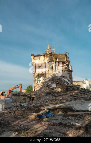 Demolizione di un edificio in rovina. L'escavatore rompe la vecchia casa danneggiata da un attacco terroristico, una guerra o un terremoto per costruire una nuova casa. Orientamento verticale Foto Stock