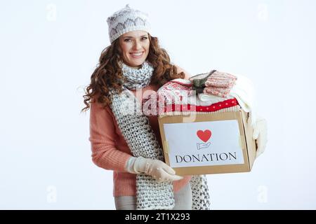 Ciao inverno. donna sorridente di mezza età con maglione, guanti, cappello e sciarpa con scatola donazione isolata su bianco. Foto Stock