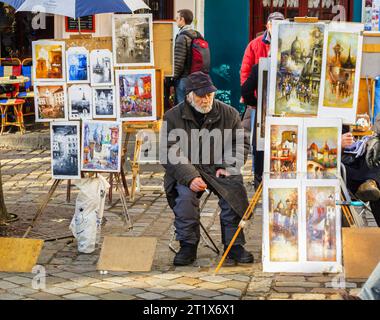 Venditore seduto che vende opere d'arte, dipinti ed espone immagini in vendita a Place du Tertre, Montmartre, XVIII arrondissement, Parigi, Francia Foto Stock