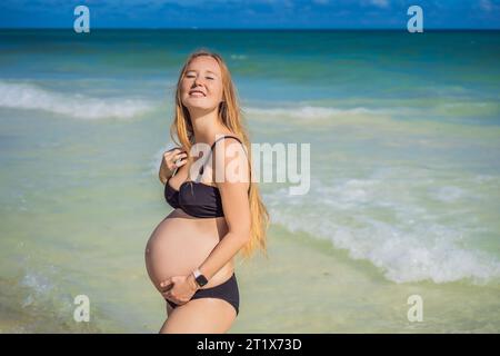 Radiosa donna incinta in costume da bagno, sullo sfondo mozzafiato di un mare turchese. Bellezza serena della maternità vicino alla riva Foto Stock