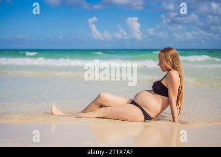 Radiosa donna incinta in costume da bagno, sullo sfondo mozzafiato di un mare turchese. Bellezza serena della maternità vicino alla riva Foto Stock