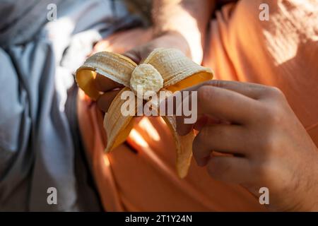 l'uomo tiene una banana in mano e la sbuccia prima di mangiarla Foto Stock