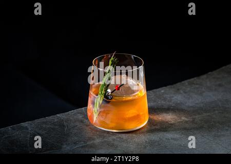 cocktail aromatico con un ciuffo di aghi di pino e ghiaccio rotondo su sfondo scuro, vista laterale Foto Stock