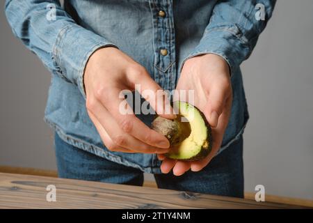 Primo piano delle mani femminili che estraggono semi dall'avocado Foto Stock