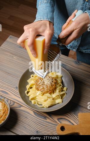 Vista ad alto angolo delle mani femminili che grattugiano il parmigiano nella pasta Foto Stock
