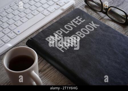 Immagine di primo piano del libro con testo MANUALE DEI DIPENDENTI circondato da una tazza di caffè e bicchieri sulla scrivania dell'ufficio Foto Stock